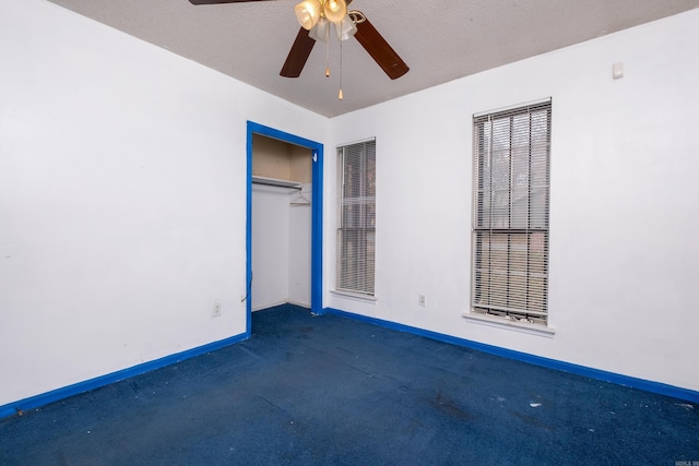 unfurnished room with ceiling fan, dark carpet, and a textured ceiling