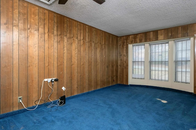 carpeted spare room with wooden walls, ceiling fan, and a textured ceiling