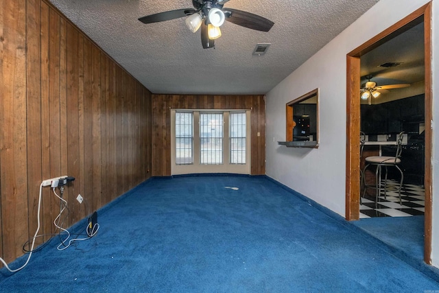 carpeted empty room featuring ceiling fan, wooden walls, and a textured ceiling