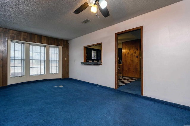 unfurnished room featuring ceiling fan, wood walls, a textured ceiling, and dark carpet