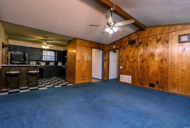 unfurnished living room with dark colored carpet, ceiling fan, wood walls, and vaulted ceiling with beams