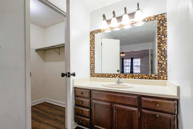 bathroom featuring vanity, ceiling fan, a textured ceiling, tasteful backsplash, and wood-type flooring