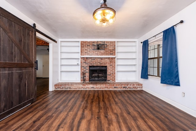 unfurnished living room featuring built in shelves, a barn door, dark hardwood / wood-style flooring, and a fireplace