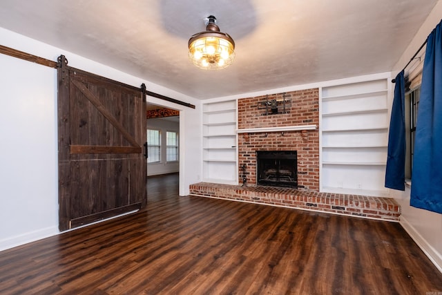 unfurnished living room with a barn door, built in shelves, dark hardwood / wood-style floors, and a brick fireplace