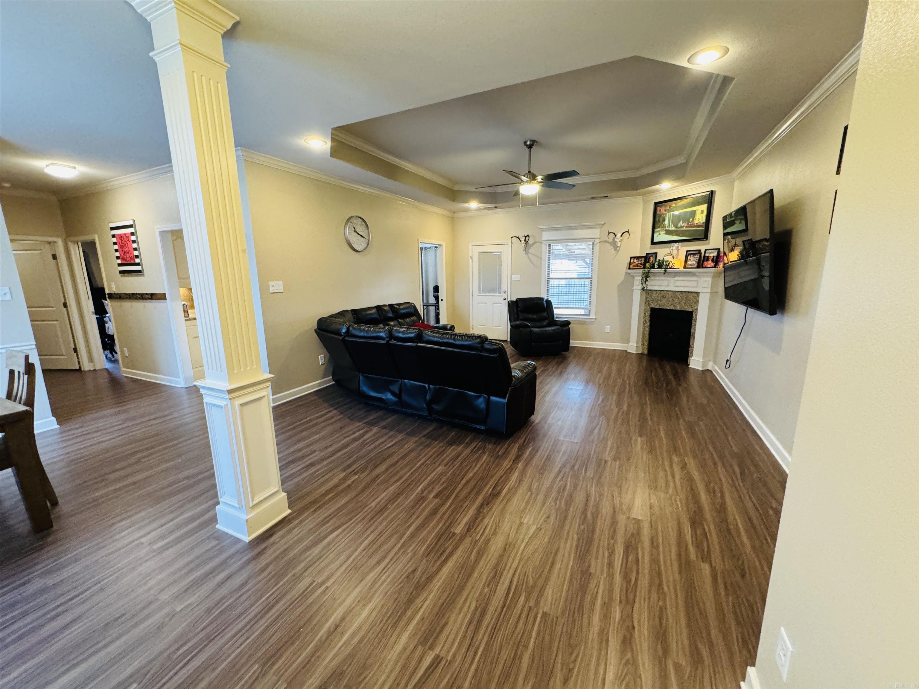 living room with decorative columns, crown molding, ceiling fan, and dark wood-type flooring