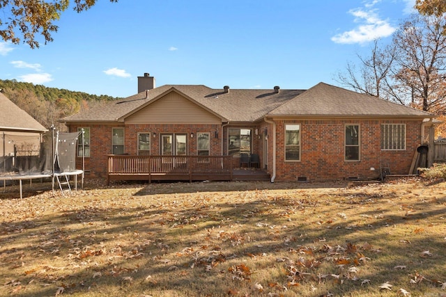 rear view of house with a trampoline, a deck, and a lawn