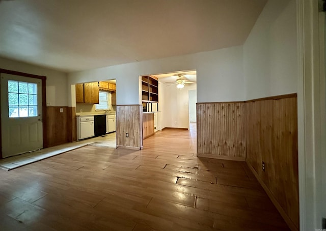 unfurnished living room featuring light wood-type flooring, ceiling fan, and wooden walls