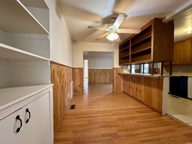 interior space with kitchen peninsula, light wood-type flooring, ceiling fan, and wooden walls