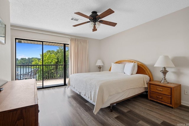 bedroom with ceiling fan, dark hardwood / wood-style floors, a textured ceiling, access to outside, and a water view