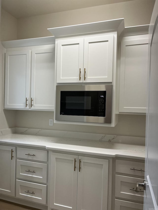 bar featuring white cabinets, white fridge, stainless steel microwave, and light stone counters