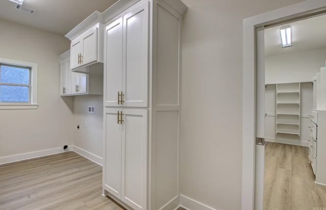 laundry room with electric dryer hookup, hookup for a washing machine, cabinets, and light wood-type flooring