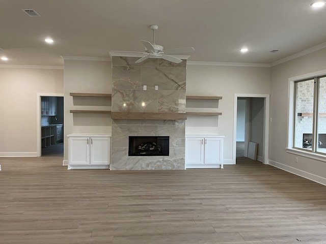 unfurnished living room with crown molding, a large fireplace, ceiling fan, and light hardwood / wood-style flooring