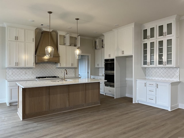 kitchen featuring a kitchen island with sink, pendant lighting, wood-type flooring, decorative backsplash, and custom range hood