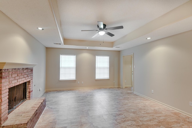 unfurnished living room featuring a tray ceiling, a brick fireplace, and ceiling fan