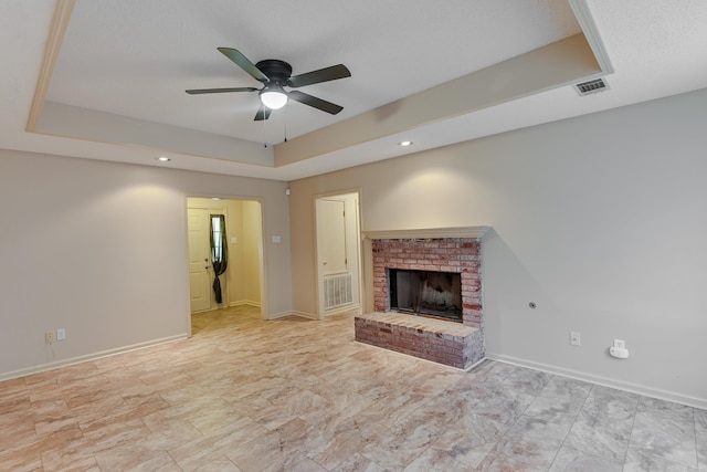 unfurnished living room with ceiling fan, a tray ceiling, and a brick fireplace