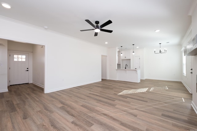 unfurnished living room with hardwood / wood-style floors, ornamental molding, ceiling fan with notable chandelier, and sink