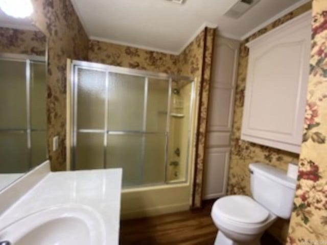 full bathroom featuring hardwood / wood-style floors, sink, toilet, and bath / shower combo with glass door