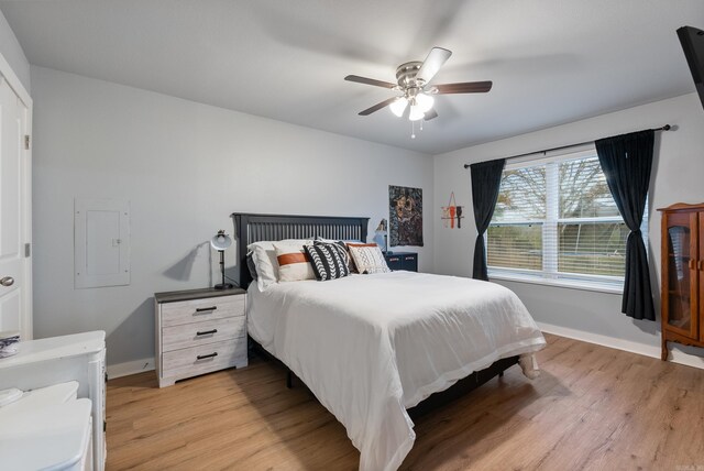 bedroom with electric panel, ceiling fan, and light wood-type flooring