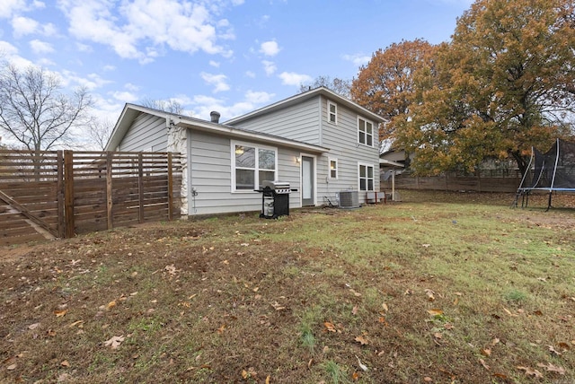 back of property with a trampoline, a lawn, and central air condition unit