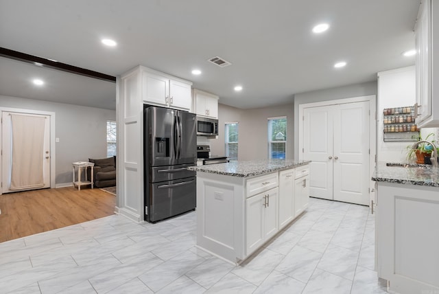 kitchen featuring white cabinets, a kitchen island, light stone counters, and appliances with stainless steel finishes