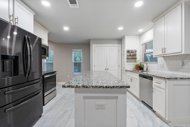 kitchen with light stone countertops, backsplash, stainless steel appliances, white cabinets, and a center island