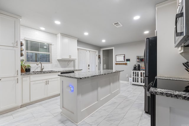 kitchen with white cabinets, black fridge, sink, light stone countertops, and a kitchen island