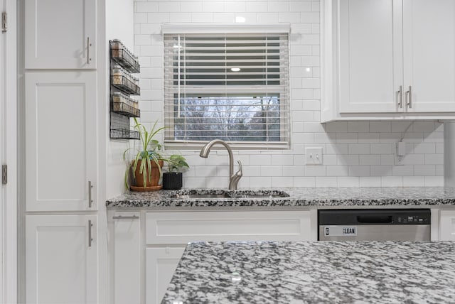 kitchen featuring white cabinets, stainless steel dishwasher, light stone countertops, and sink