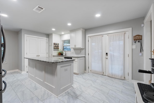 kitchen with a center island, light stone countertops, white cabinetry, and tasteful backsplash