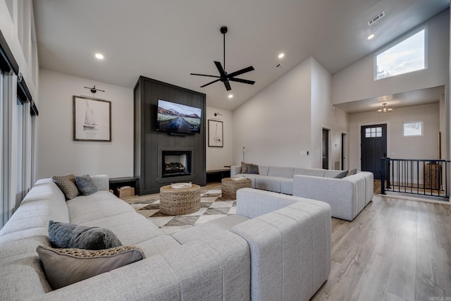 living room featuring ceiling fan, a large fireplace, high vaulted ceiling, and light wood-type flooring