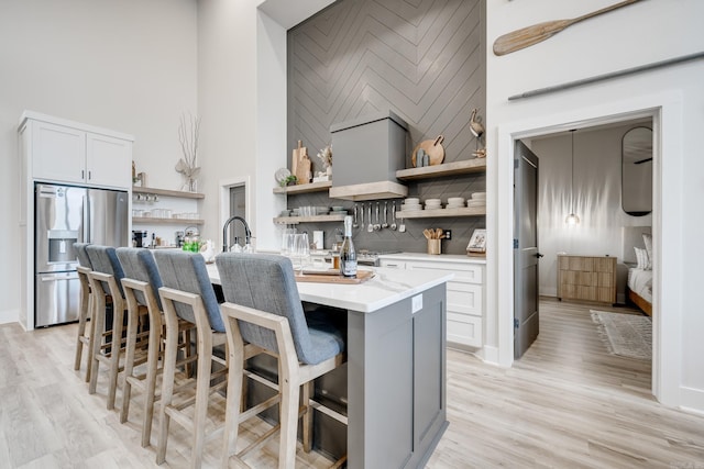 kitchen with stainless steel fridge with ice dispenser, light hardwood / wood-style flooring, a towering ceiling, a kitchen island with sink, and a breakfast bar