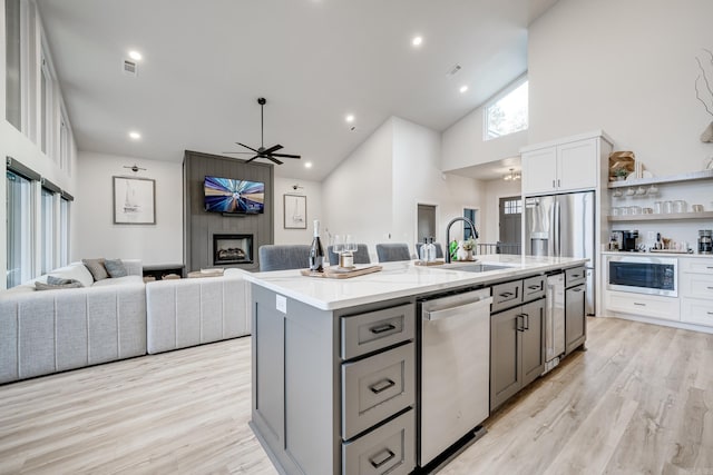 kitchen featuring high vaulted ceiling, a center island with sink, white cabinets, a large fireplace, and stainless steel appliances