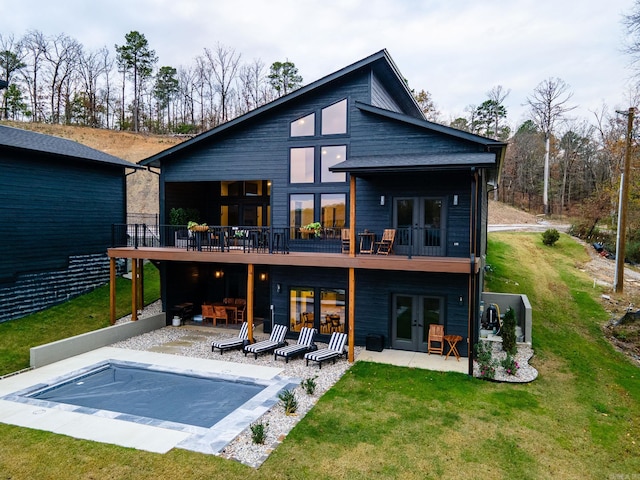 rear view of property featuring a patio area, a covered pool, a yard, and french doors