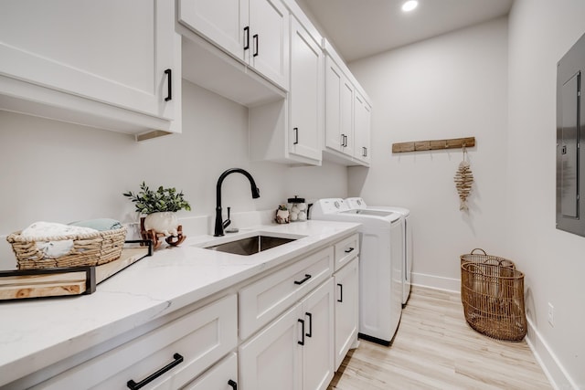 clothes washing area with cabinets, electric panel, sink, washing machine and dryer, and light hardwood / wood-style floors