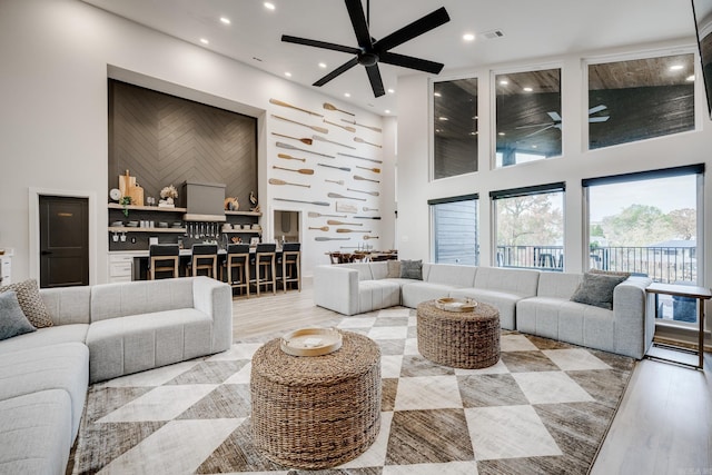 living room featuring hardwood / wood-style flooring, ceiling fan, and a towering ceiling