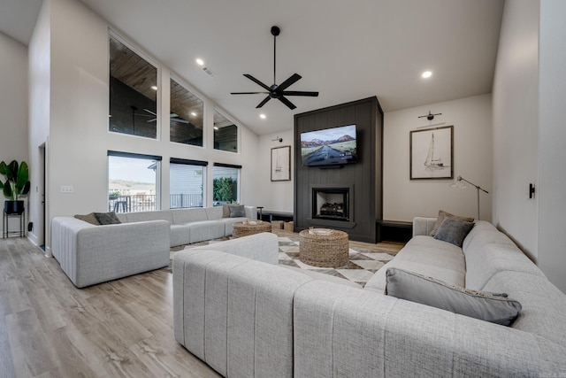 living room featuring ceiling fan, a large fireplace, high vaulted ceiling, and light hardwood / wood-style flooring