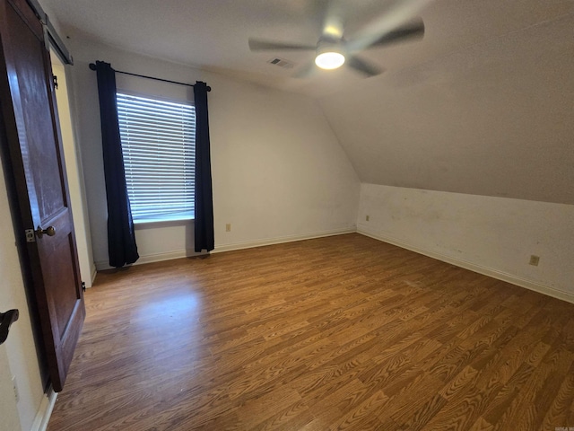 bonus room with ceiling fan, a barn door, dark hardwood / wood-style flooring, and vaulted ceiling