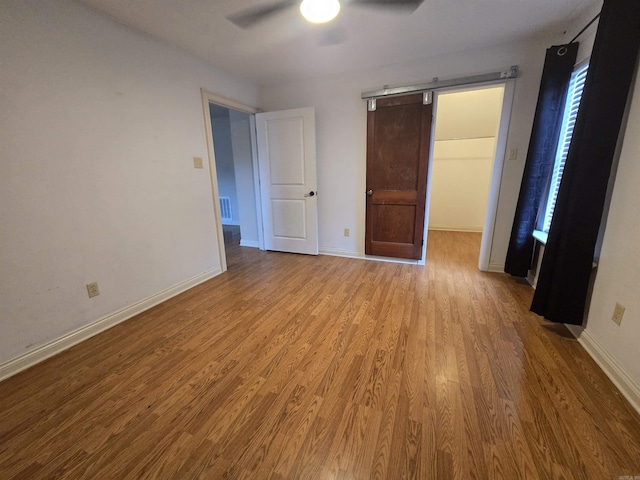 unfurnished bedroom featuring ceiling fan, a spacious closet, and light wood-type flooring