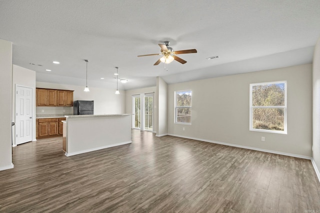 unfurnished living room with a textured ceiling, ceiling fan, a healthy amount of sunlight, and dark wood-type flooring