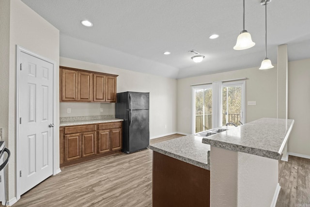 kitchen featuring black fridge, sink, decorative light fixtures, light hardwood / wood-style floors, and a kitchen island