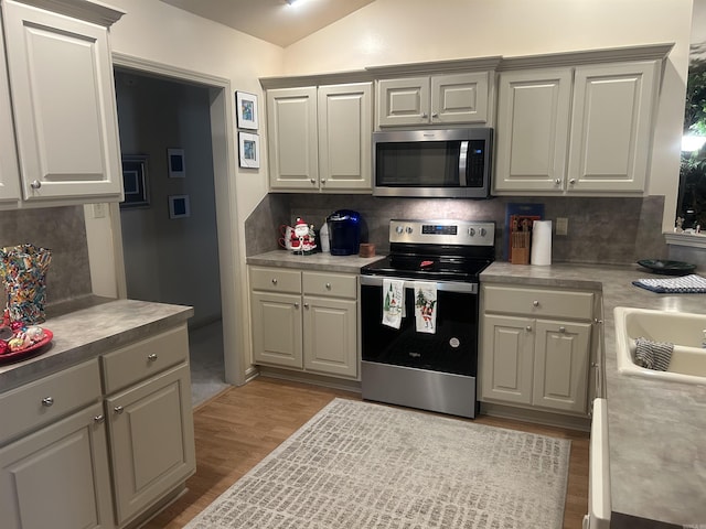 kitchen with lofted ceiling, backsplash, light hardwood / wood-style flooring, gray cabinets, and stainless steel appliances