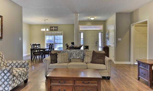 living room with a textured ceiling, decorative columns, dark hardwood / wood-style floors, and an inviting chandelier