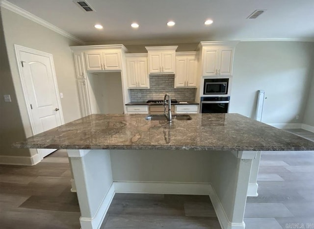 kitchen featuring appliances with stainless steel finishes, a large island with sink, dark stone countertops, and sink