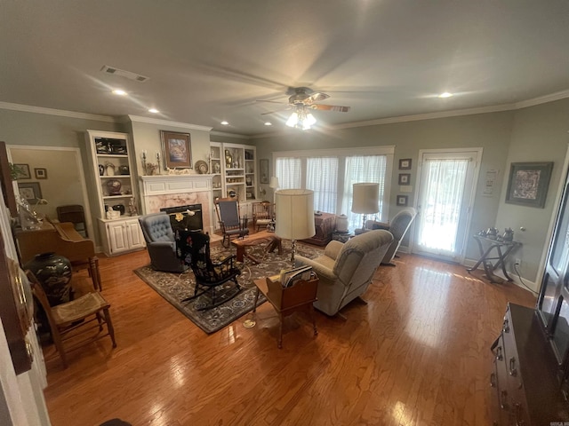 living room featuring ceiling fan, a fireplace, light wood-type flooring, and ornamental molding