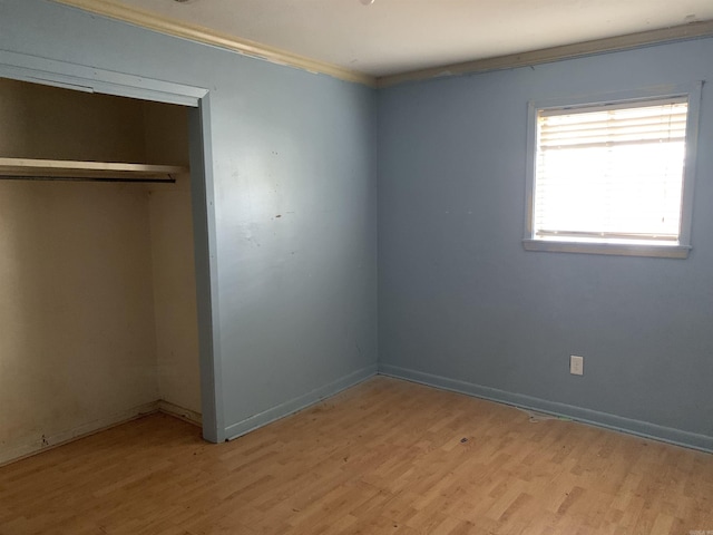 unfurnished bedroom featuring light hardwood / wood-style floors, crown molding, and a closet