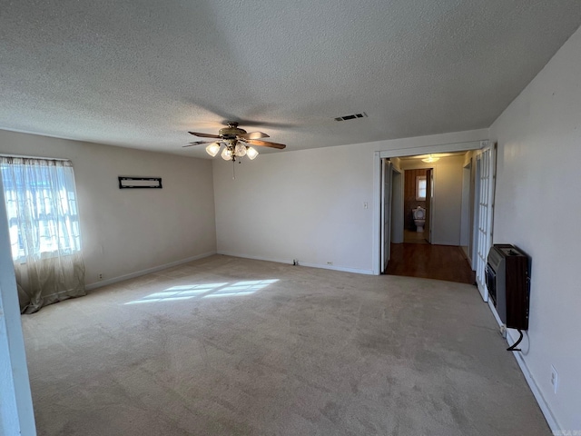 empty room featuring heating unit, light carpet, ceiling fan, and a textured ceiling