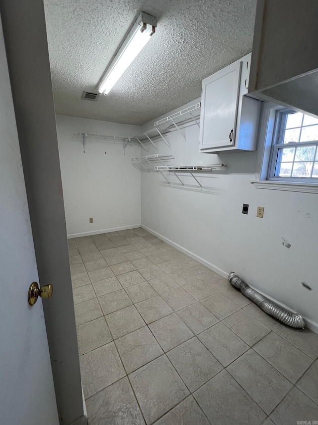 washroom with cabinets, light tile patterned floors, a textured ceiling, and hookup for an electric dryer