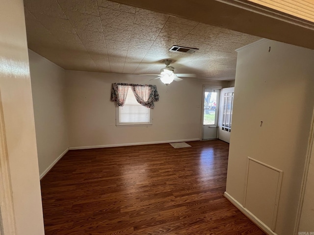 empty room featuring a wealth of natural light, ceiling fan, and dark wood-type flooring