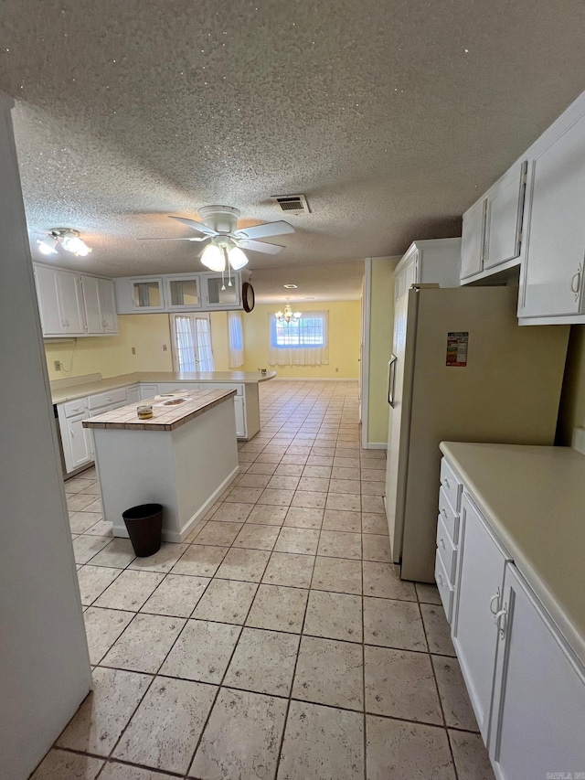 kitchen with a textured ceiling, ceiling fan, white refrigerator, white cabinetry, and light tile patterned flooring