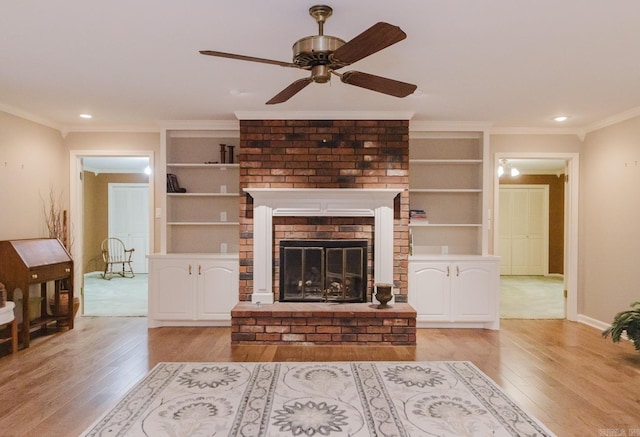 living room featuring a fireplace, built in shelves, light hardwood / wood-style floors, ceiling fan, and crown molding