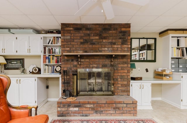 tiled living room with a brick fireplace, ceiling fan, and a paneled ceiling